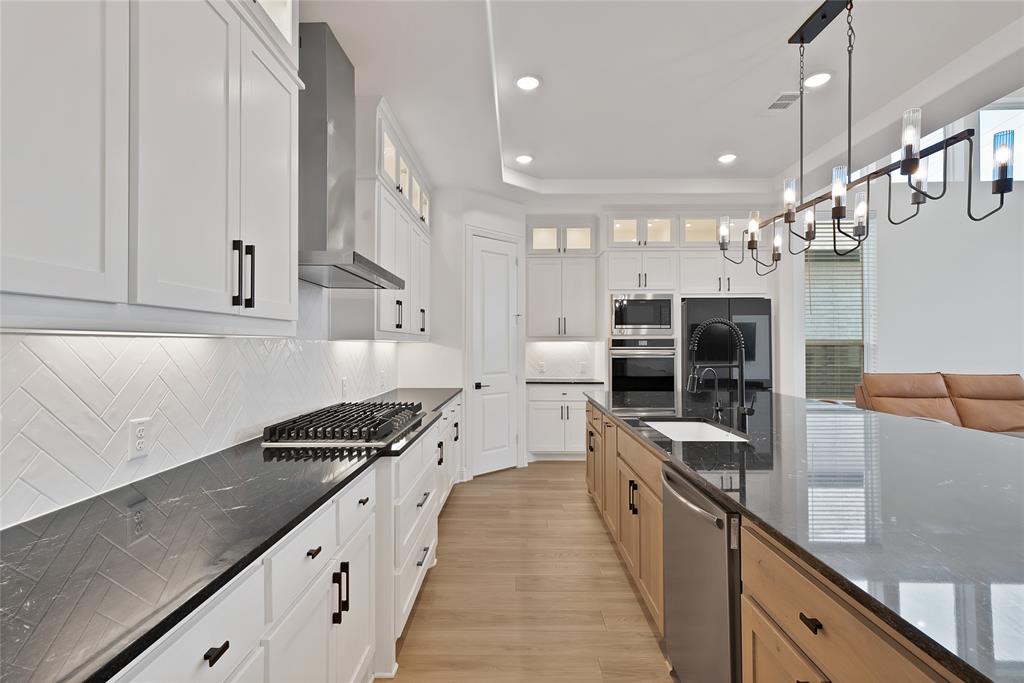 Kitchen featuring white shaker-style cabinetry, dark stone countertops, herringbone-pattern tile backsplash, stainless steel built-in double wall ovens, and a multi-light industrial-style pendant fixture