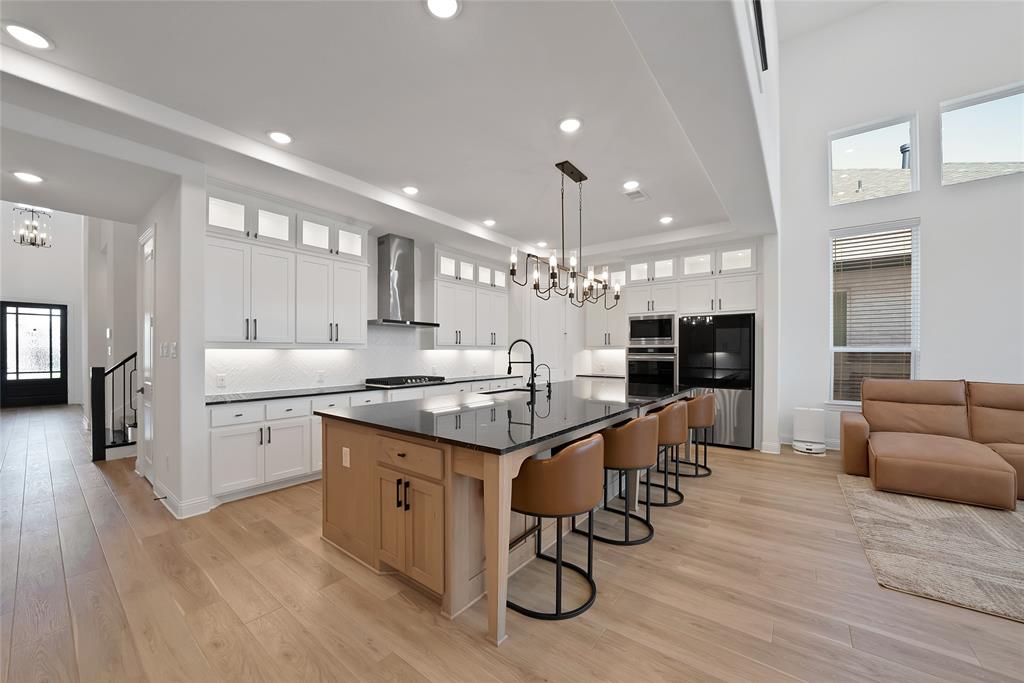 Kitchen featuring shaker-style cabinetry with glass-front uppers, a central island with wood-finish base, dark stone countertops, recessed lighting, and high ceilings