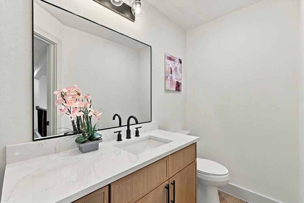 Vanity featuring a light wood-finish cabinet, white surface with veining, and a black-framed rectangular mirror, accented by a matte black faucet and multi-bulb industrial-style lighting