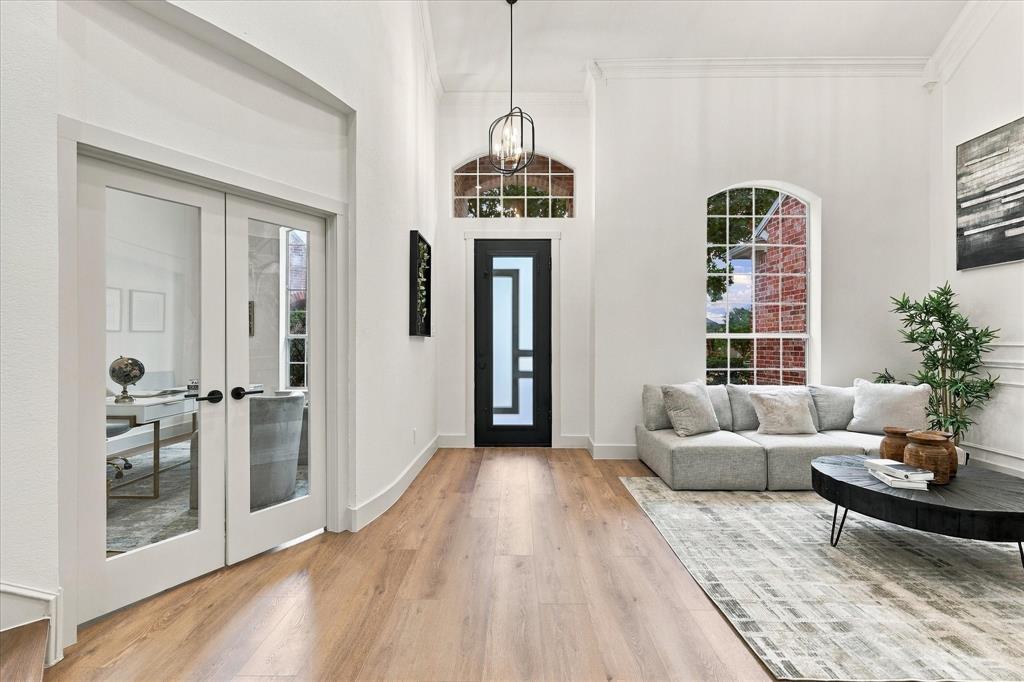 Foyer featuring high ceilings, wood-finish flooring, a contemporary front door with geometric glass panels, arched window, and dual glass-panel French doors Foyer featuring high ceilings, wood-finish flooring, a contemporary front door with geometric glass panels, arched window, and dual glass-panel French doors