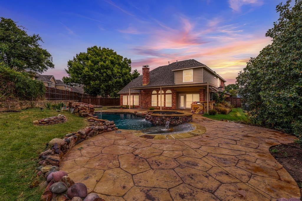 Rear exterior featuring a brick and siding facade, covered patio, stone-accented pool with integrated spa, and extensive flagstone hardscaping Rear exterior featuring a brick and siding facade, covered patio, stone-accented pool with integrated spa, and extensive flagstone hardscaping