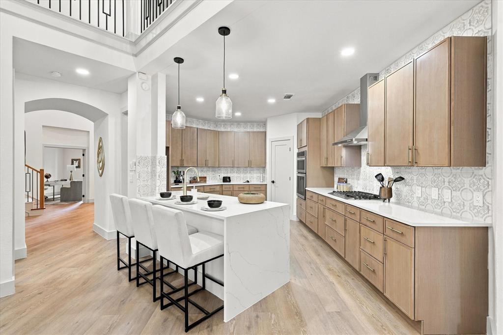 Kitchen featuring a large central island with a stone countertop, flat-panel wood cabinetry, patterned tile backsplash, stainless steel gas cooktop with range hood, and wood-finish flooring