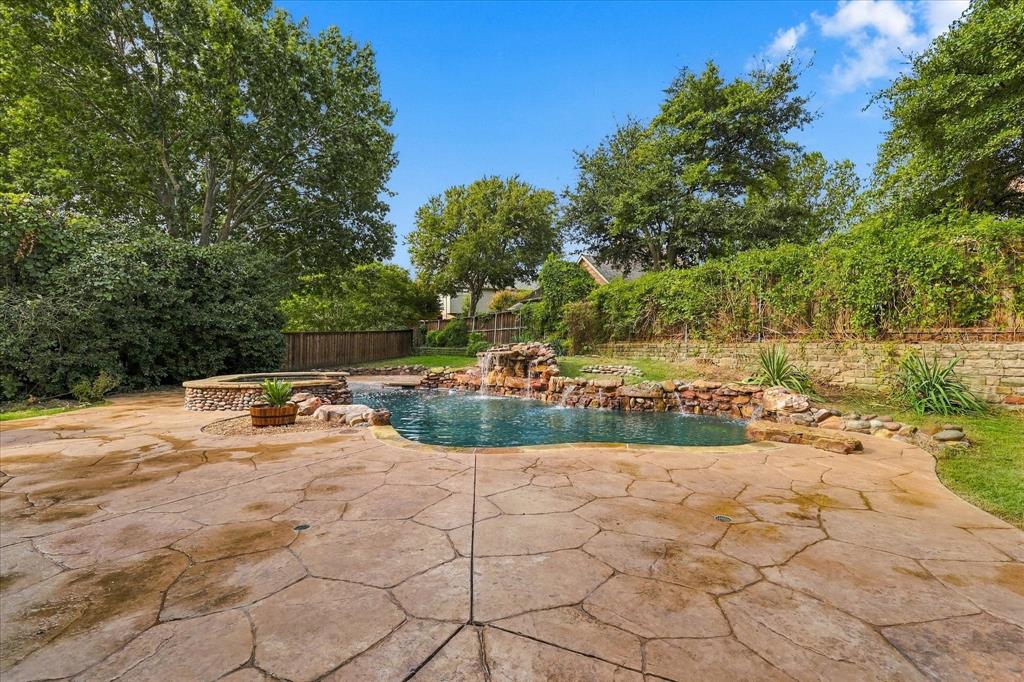 Outdoor oasis featuring a flagstone patio, natural rock-accented pool, integrated stone waterfall, raised spa, and stone retaining wall
