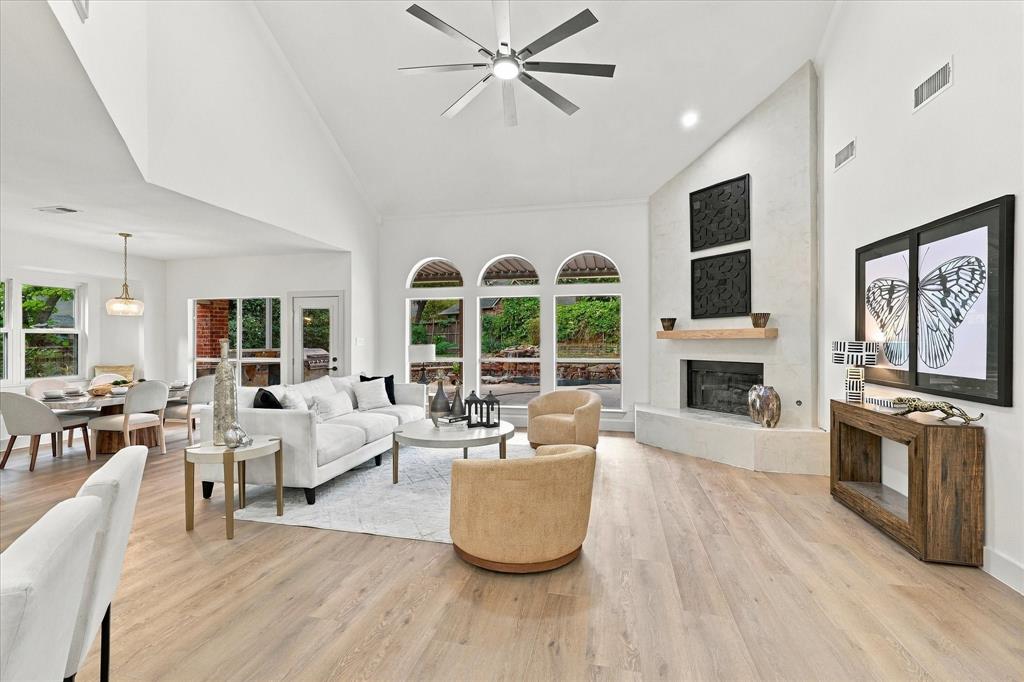 Vaulted ceilings with a multi-blade ceiling fan, expansive wood-finish flooring, floor-to-ceiling stone-faced fireplace with a natural wood mantel, and arched windows