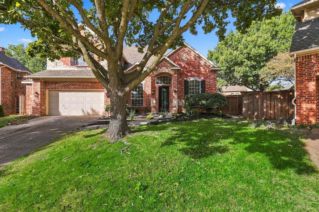 Red brick exterior featuring a multi-gabled roofline, arched entryway, attached two-car garage, mature landscaping, and wood privacy fencing Red brick exterior featuring a multi-gabled roofline, arched entryway, attached two-car garage, mature landscaping, and wood privacy fencing