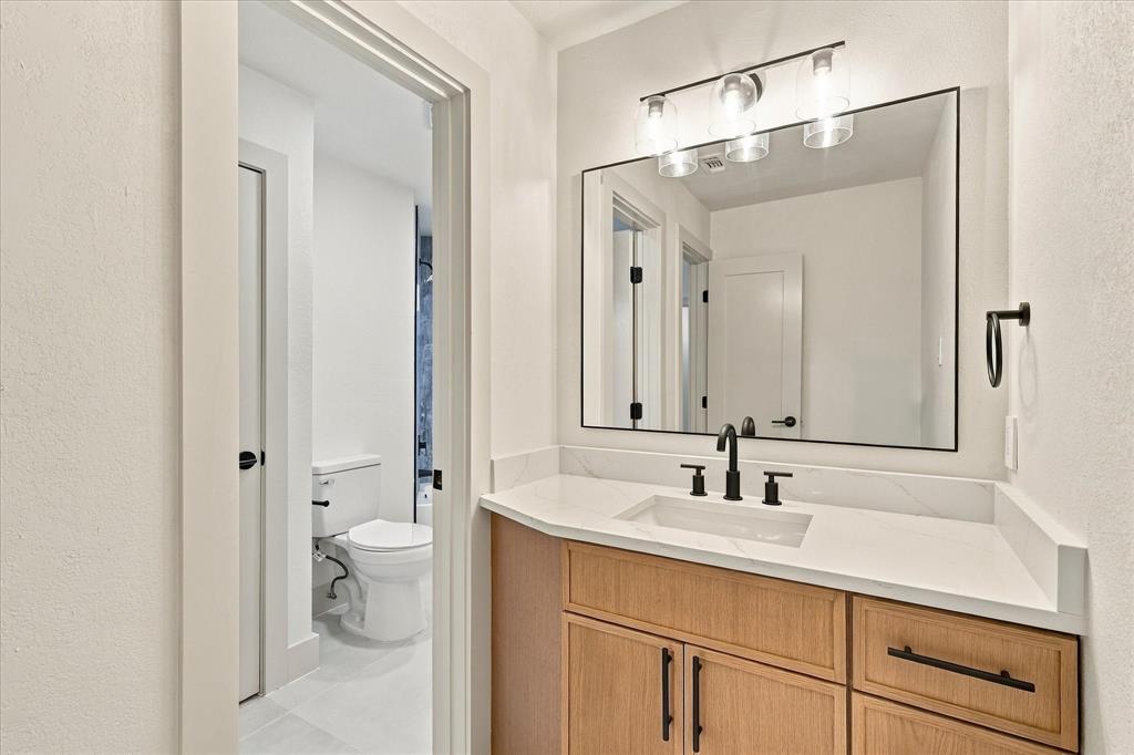 Bathroom vanity featuring a light wood-finish cabinet, white countertop with integrated rectangular sink, matte black widespread faucet, and a modern three-light fixture above a rectangular mirror