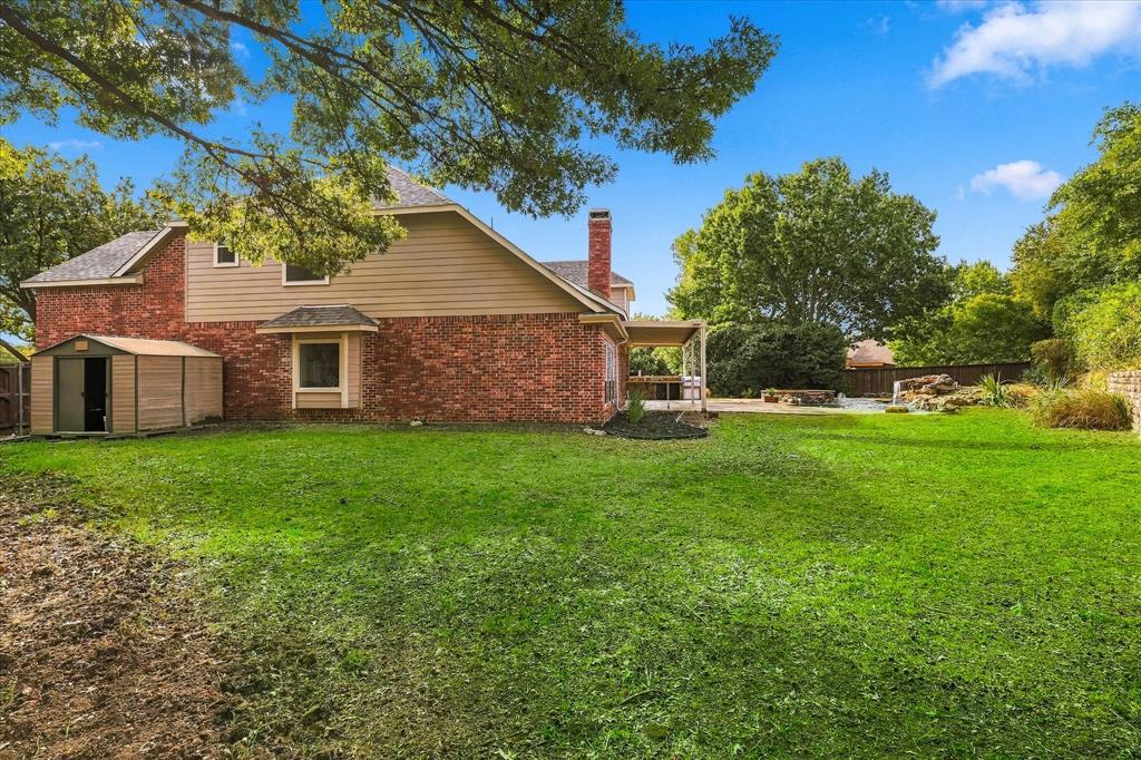 Expansive backyard featuring a brick and siding exterior, a masonry chimney, a covered patio, and a stone-accented water feature