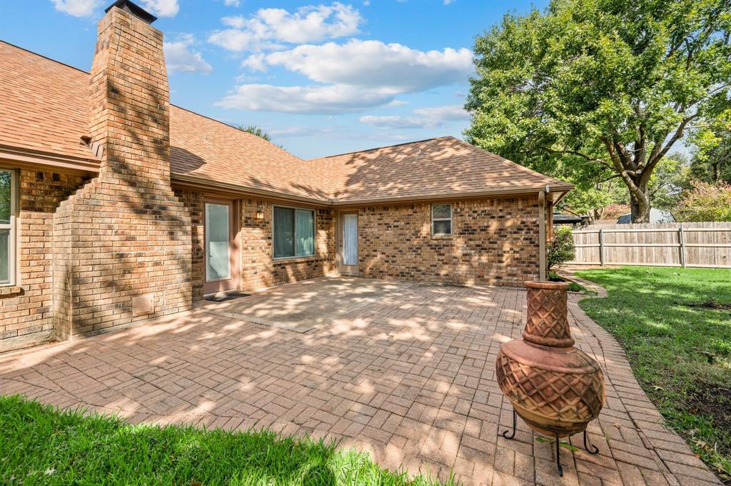 Rear exterior featuring a brick facade, chimney, herringbone-patterned paved patio, and perimeter wood fencing