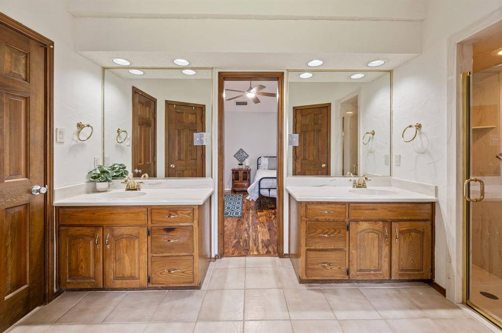 Dual-vanity bathroom featuring solid-wood cabinetry, stone-finish countertops, recessed lighting, and a glass-enclosed shower with gold-tone hardware