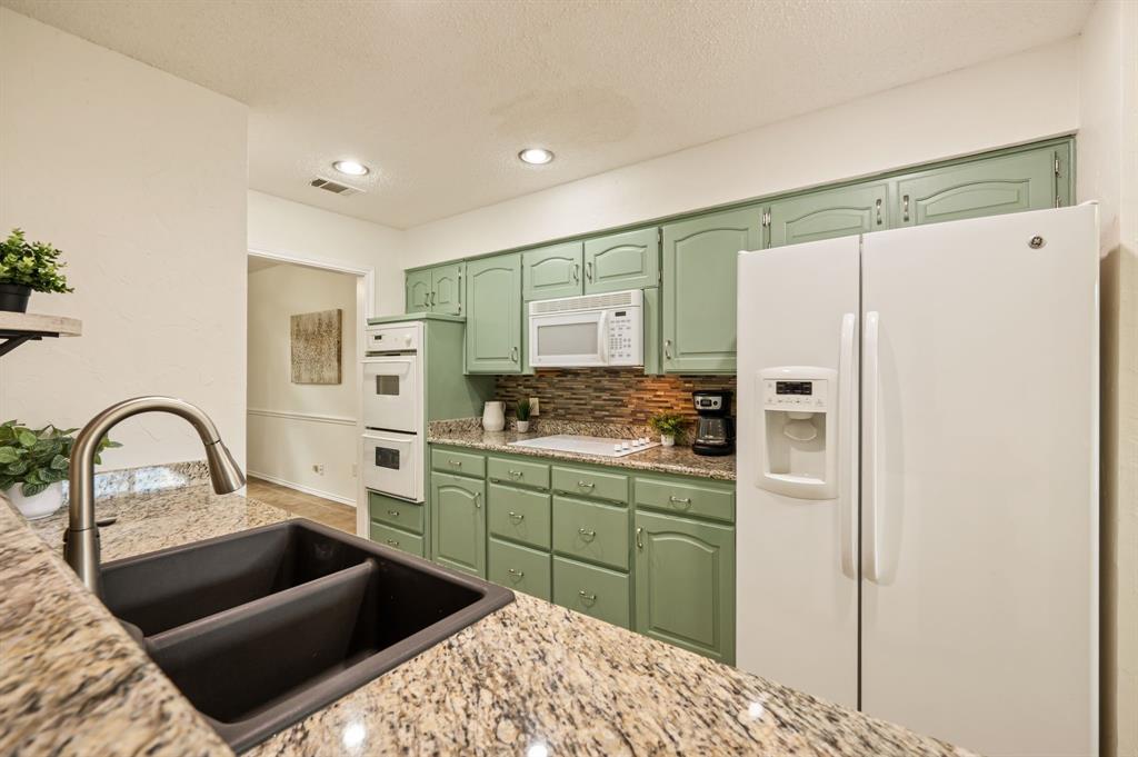 Kitchen featuring sage-toned cabinetry, multi-tonal stone backsplash, speckled stone-finish countertops, built-in dual wall oven, and a double-basin undermount sink with a gooseneck faucet