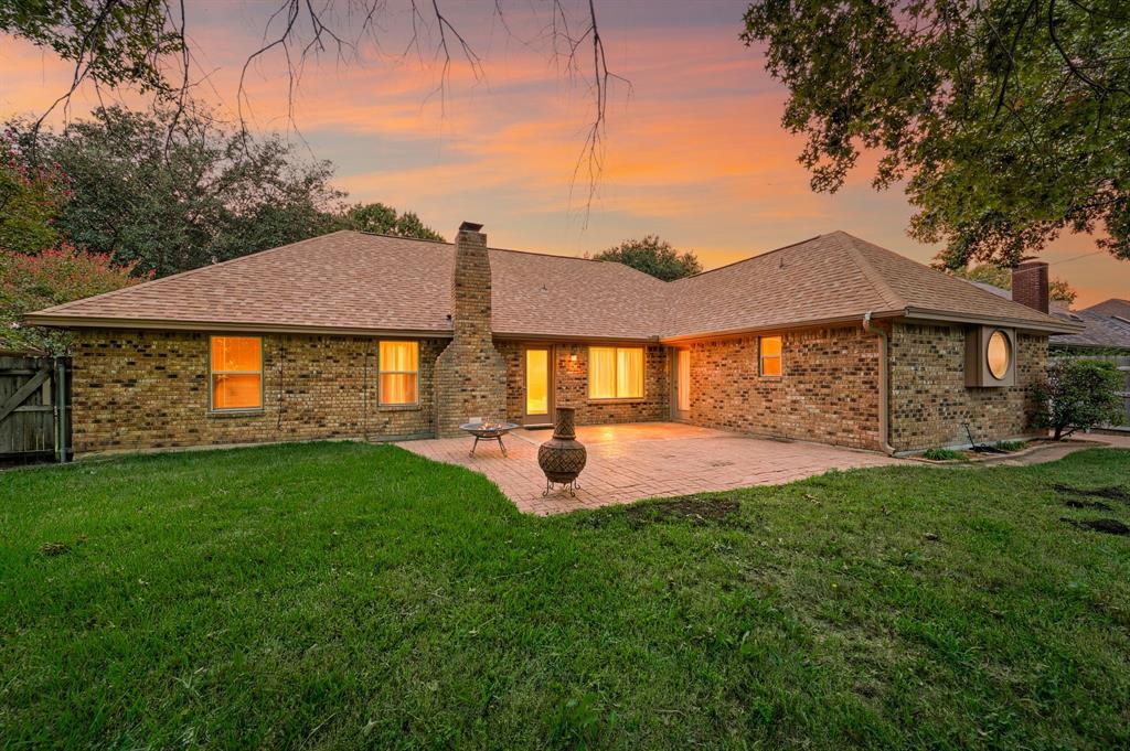 Brick exterior featuring a masonry chimney, paved rear patio, composition shingle roof, and exterior circular window