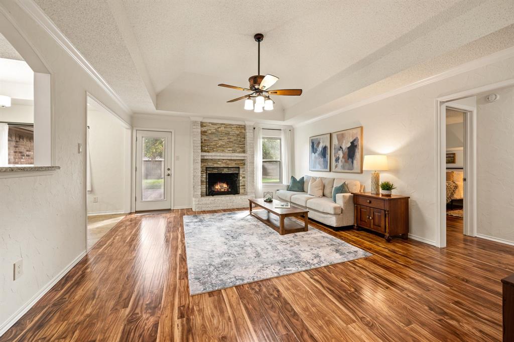 Living area featuring wood-finish flooring, a vaulted ceiling with an integrated ceiling fan, and a floor-to-ceiling stone-faced fireplace with a mantel