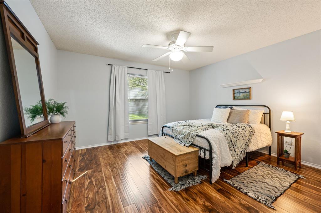 Bedroom featuring wood-finish flooring, a central ceiling fan with an integrated light fixture, and a built-in wall shelf