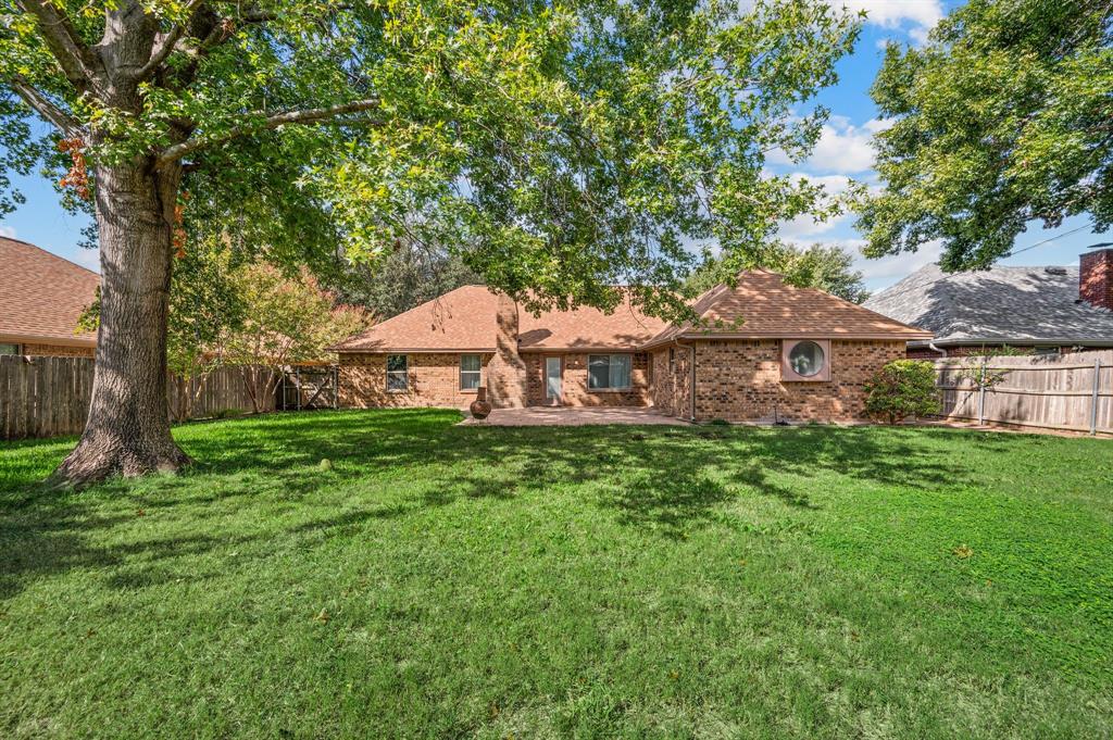 Spacious backyard featuring a brick exterior, mature trees, wood privacy fencing, and a stone patio
