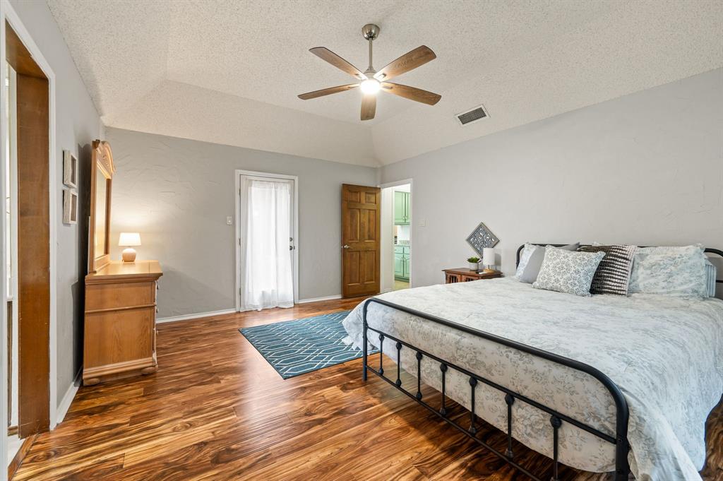 Vaulted ceiling featuring a five-blade ceiling fan with integrated lighting, wood-finish flooring, and a glass-paneled exterior door