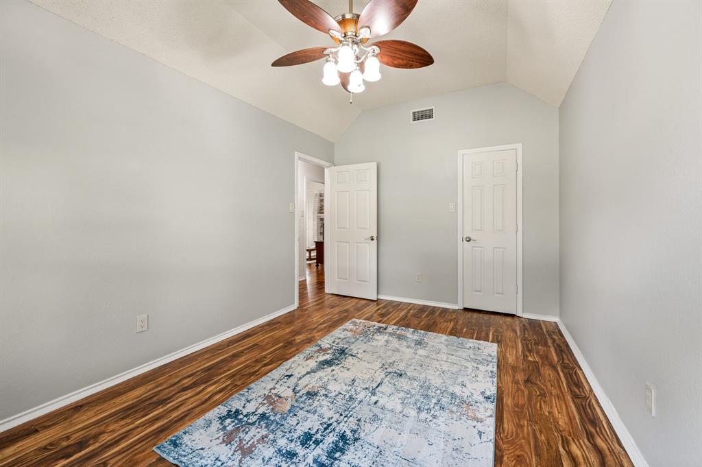 Vaulted ceiling featuring a central five-blade light fixture, wood-finish flooring, and two six-panel interior doors