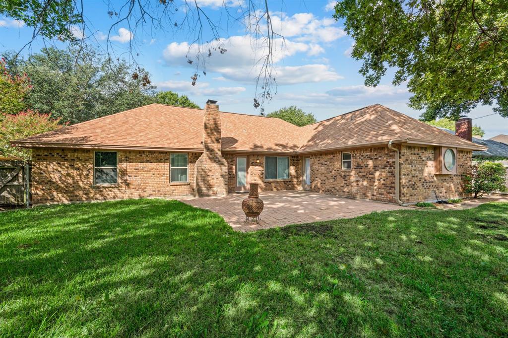 Brick exterior featuring a masonry chimney, expansive paved patio, and mature trees