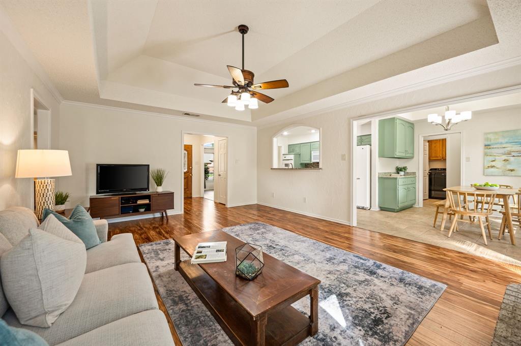Living area featuring tray ceilings, a ceiling fan with integrated lighting, and wood-finish flooring