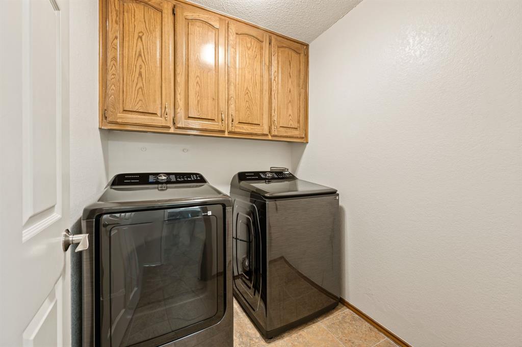 Laundry area featuring built-in wood-finish cabinetry, neutral wall surfaces, and tile flooring