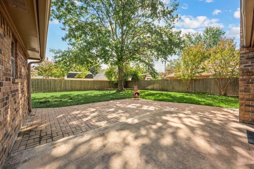 Rear exterior patio featuring brick pavers, concrete slab, brick masonry siding, wood privacy fencing, and mature trees