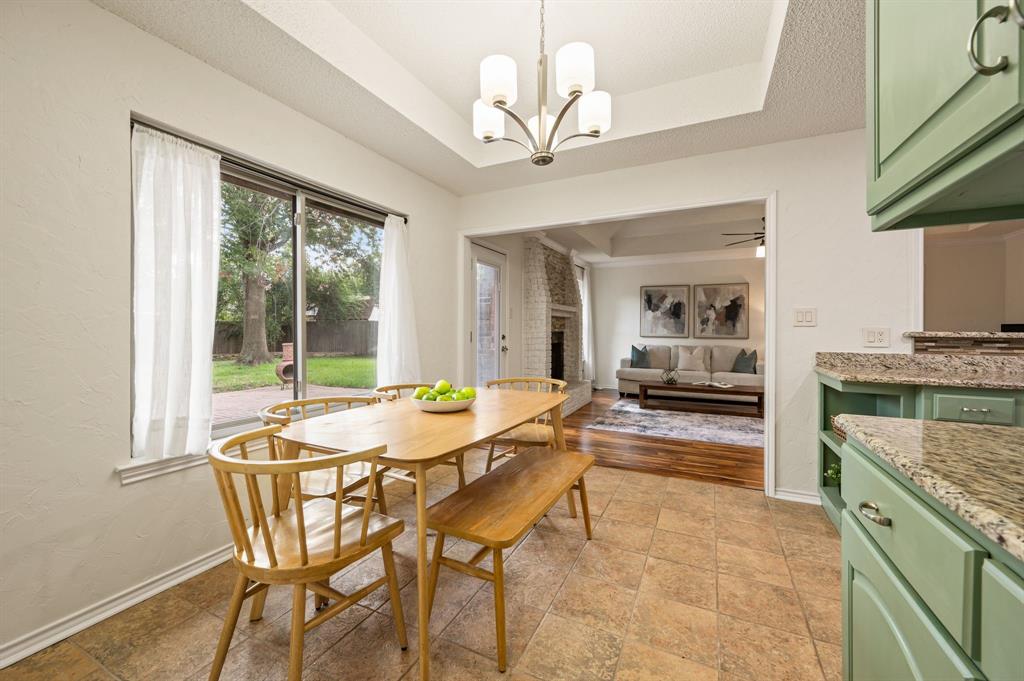 Dining area featuring a tray ceiling with a multi-arm chandelier, light-toned tile flooring, sage green cabinetry with stone-finish countertops, and sliding glass doors