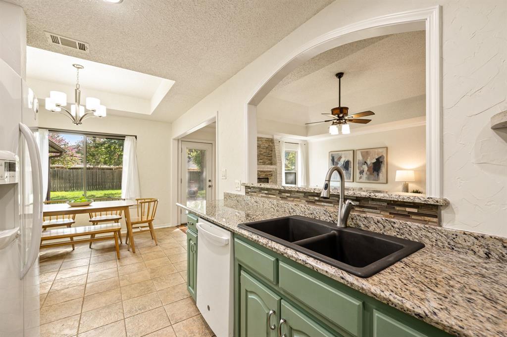 Kitchen featuring stone-finish countertops, a double-basin undermount sink with a gooseneck faucet, tile flooring, and a pass-through window with a decorative tiled backsplash