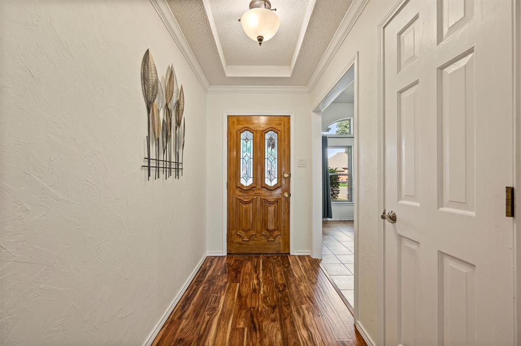 Foyer featuring wood-finish flooring, a recessed tray ceiling, a central dome-style light fixture, and a solid wood front door with decorative glass inserts