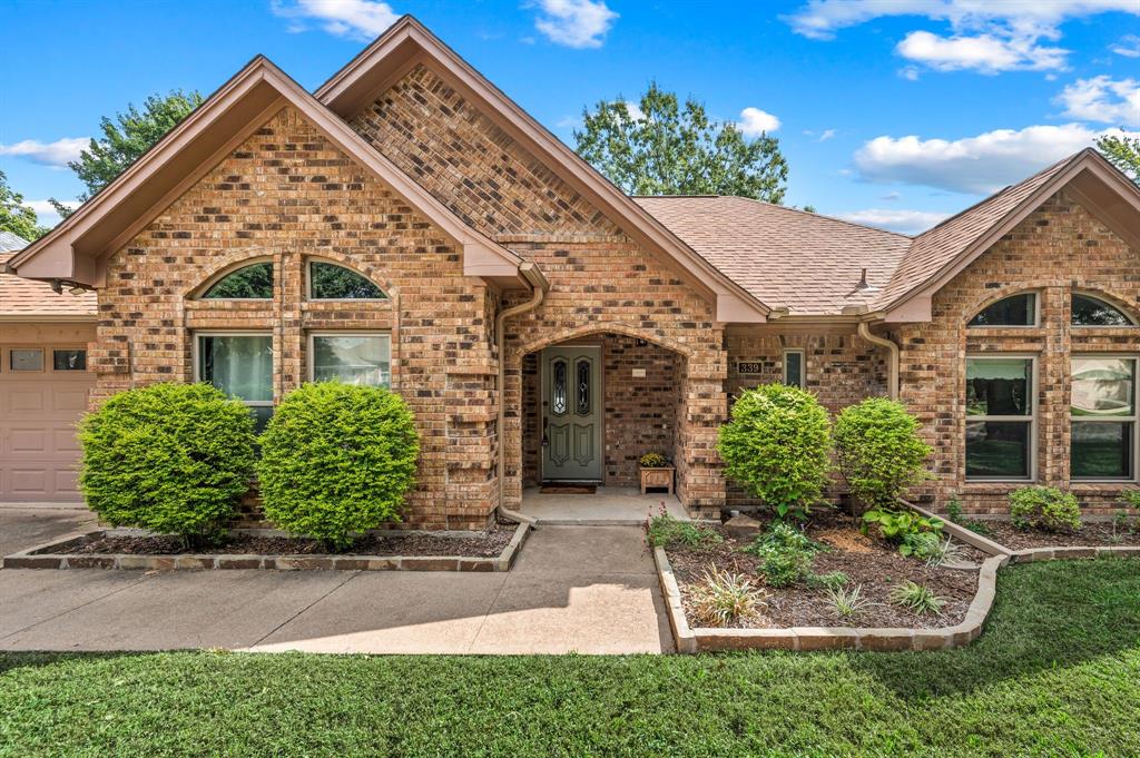 Multi-gabled brick exterior featuring arched windows, a recessed covered entryway, and stone-bordered landscaping beds