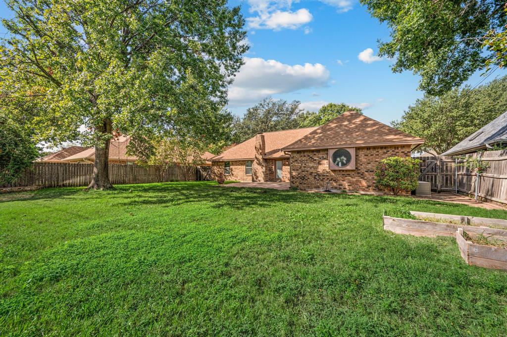Expansive backyard featuring a brick exterior, mature trees, a circular accent window, and raised wooden planting beds