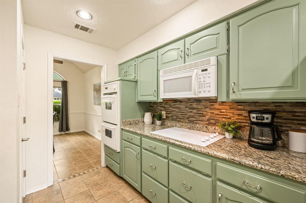 Kitchen featuring sage green cabinetry, stone-patterned countertops, mosaic tile backsplash, white built-in double wall oven, and white electric cooktop