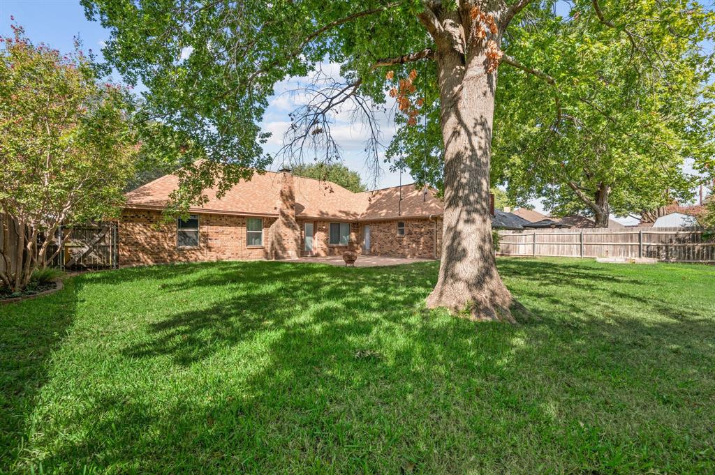 Expansive backyard featuring a brick exterior, stone-paved patio, mature trees, and a wood privacy fence