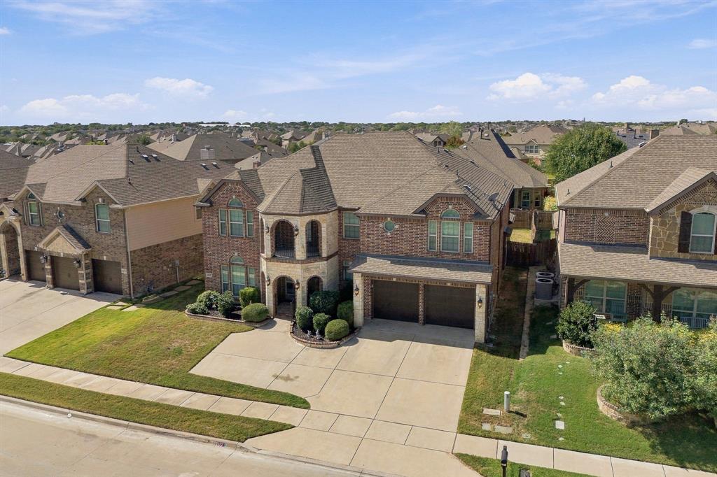 Two-story brick and stone facade featuring a covered front porch, dual-level arched entry, attached two-car garage, and a concrete driveway