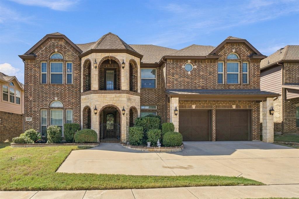 Multi-level brick exterior featuring natural stone accents, a covered dual-level arched entryway, arched window detailing, and an attached two-car garage