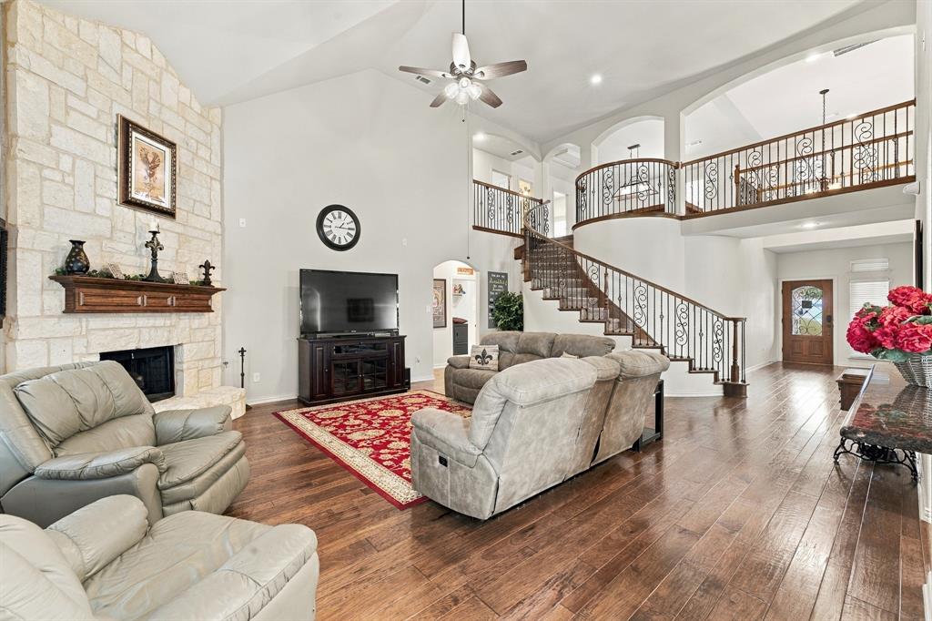 Vaulted ceilings, floor-to-ceiling stone fireplace with a wood mantel, wood-finish flooring, and a curved staircase featuring intricate metal balusters