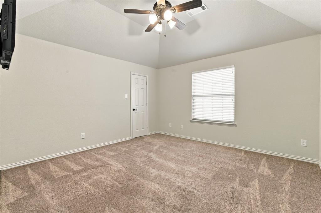 Vaulted ceiling featuring a central multi-blade ceiling fan with integrated light fixture, neutral wall palette, wall-to-wall carpeting, and a single-pane window with horizontal blinds