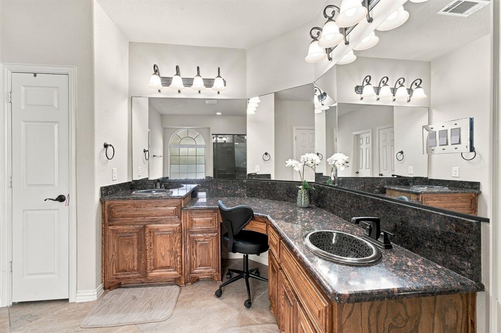 Dual-sink vanity featuring stained wood cabinetry, stone countertops, integrated oval basins, and wall-mounted light fixtures