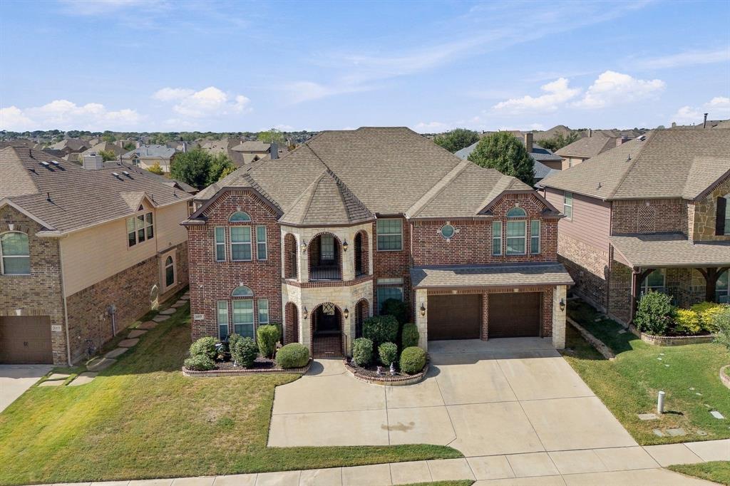 Two-story brick and stone facade featuring a turret-style architectural element, two-level covered porch, multi-gabled roofline, and attached two-car garage