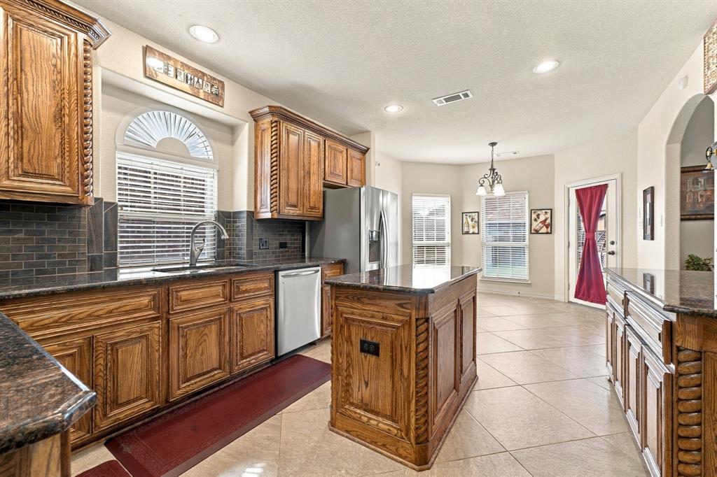 Kitchen featuring custom wood cabinetry, a center island, dark stone countertops, tile flooring, and an arched window