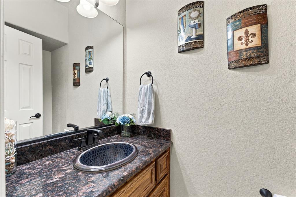 Stone-finish countertop featuring an oval drop-in sink, dark-finish faucet hardware, large wall-mounted mirror, and wood-finish cabinetry