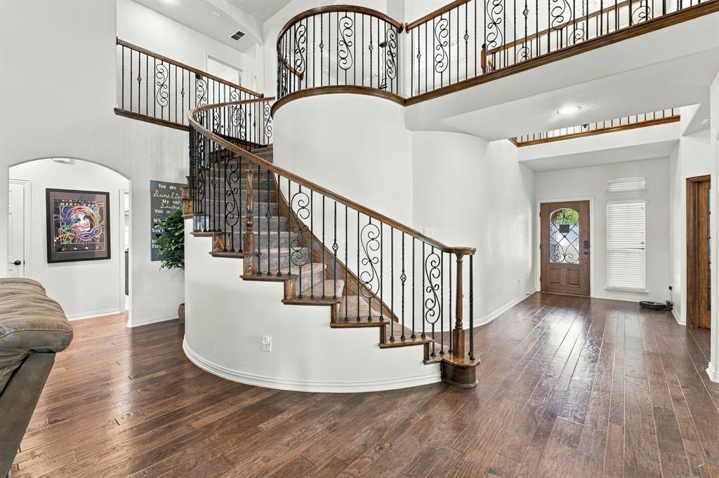 Grand foyer featuring a curved staircase with wood handrails, intricate metal balusters, wood-finish flooring, and a stained wood entry door with decorative glass inlay
