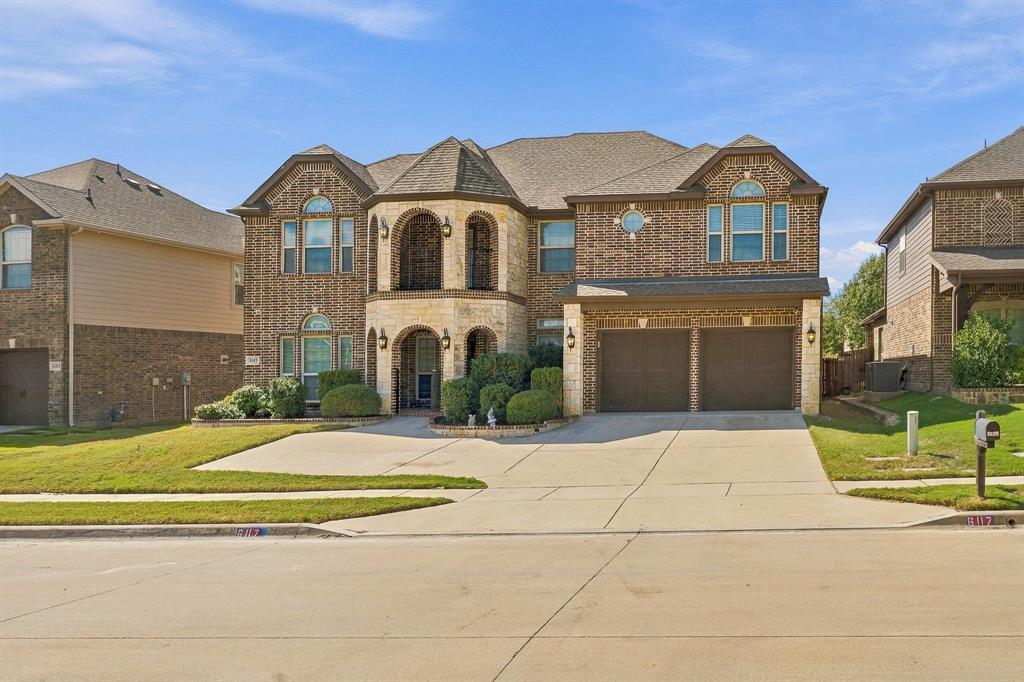 Two-story brick exterior featuring light-colored stone accents, a multi-gabled roofline, an arched covered entryway, and an attached two-car garage
