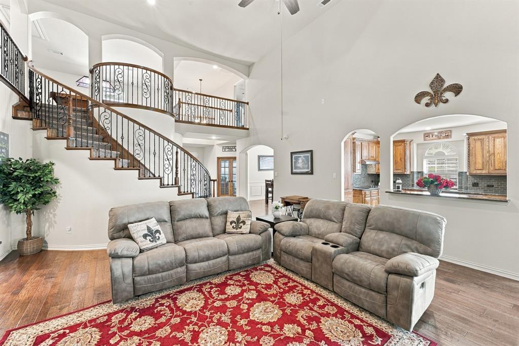 Two-story living area featuring vaulted ceilings, a curved staircase with decorative wrought-iron railings, wood-finish flooring, and arched architectural openings