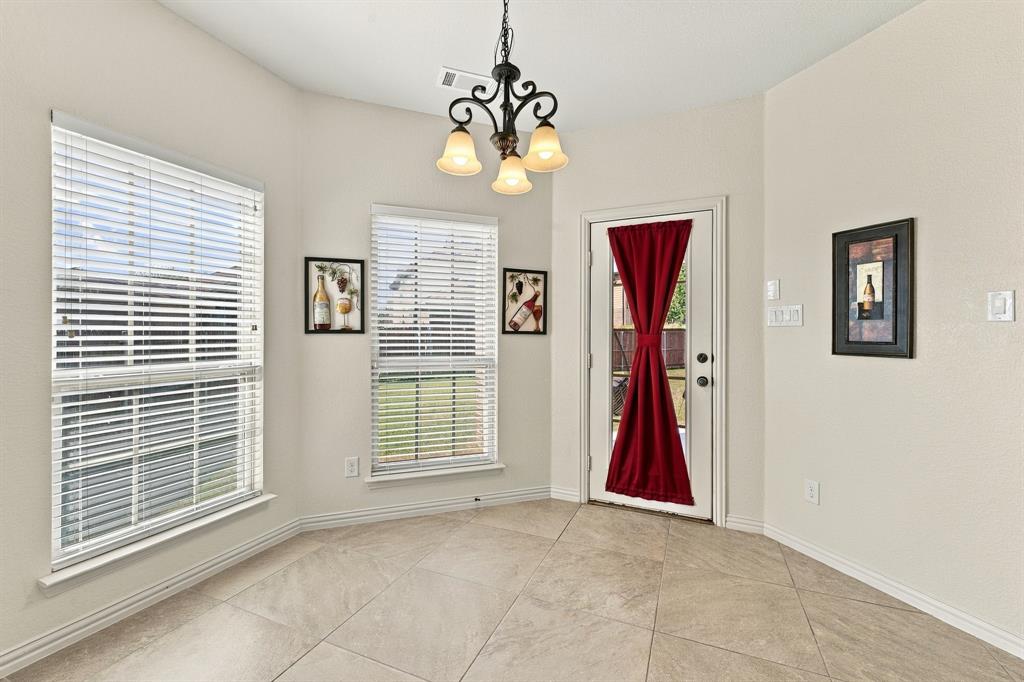 Neutral-toned tile flooring set on a diagonal pattern, three-light metal chandelier with scrolled detailing, dual windows with horizontal blinds, and a glass-paneled exterior door
