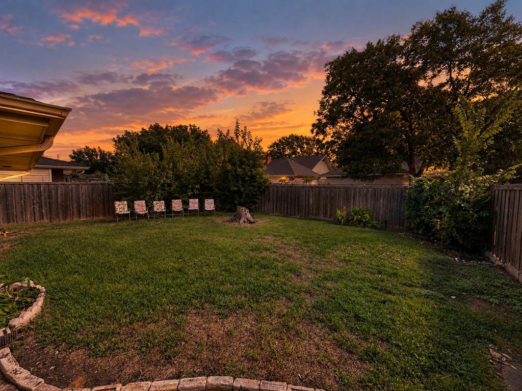 Expansive backyard featuring a manicured lawn, stone-border garden beds, mature trees, and perimeter wood fencing