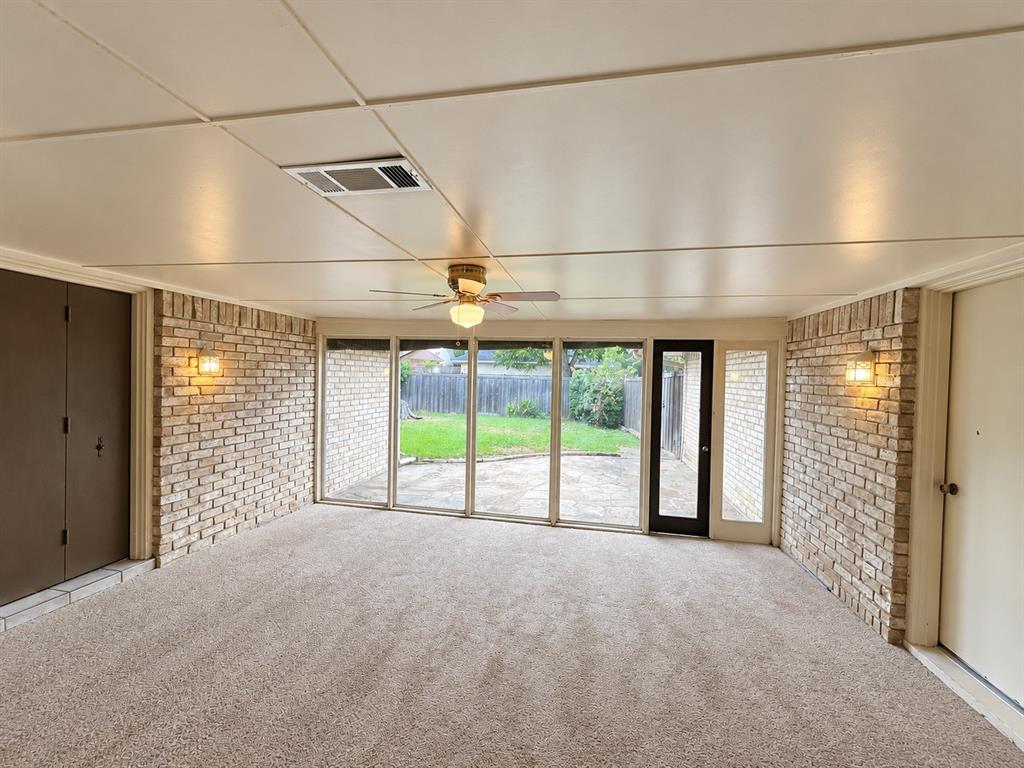 Enclosed sunroom featuring exposed brick walls, expansive floor-to-ceiling windows, wall-mounted lighting, and a ceiling fan