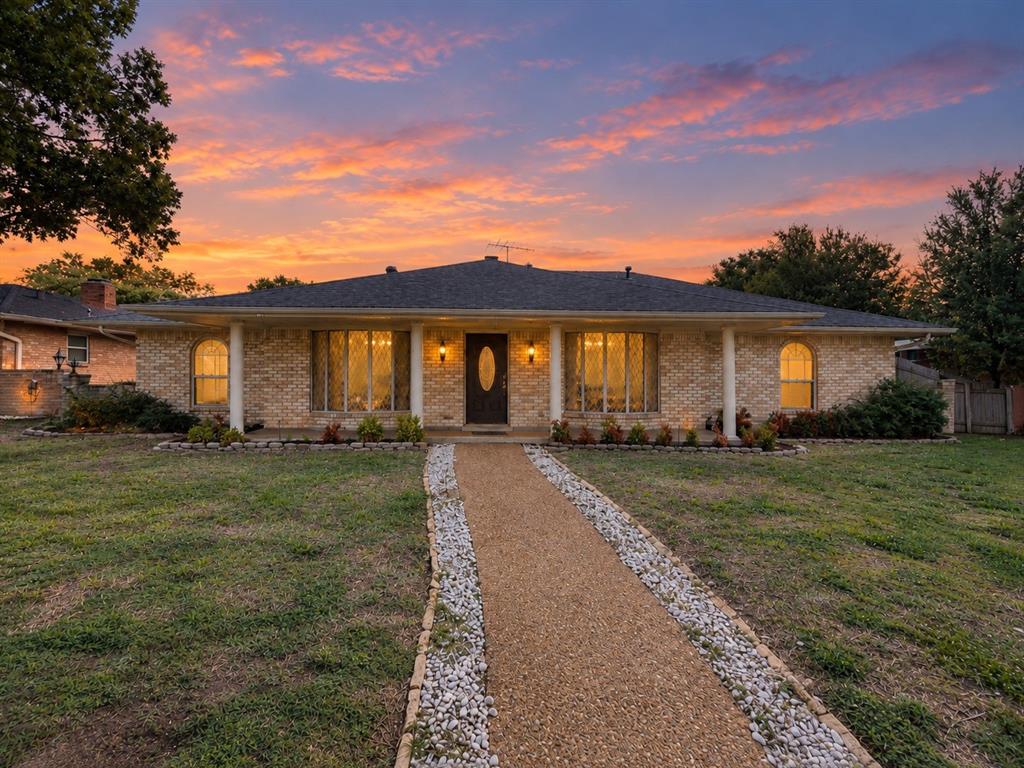 Single-story brick exterior featuring a covered front porch with white columns, arched window detailing, and a stone-bordered gravel walkway