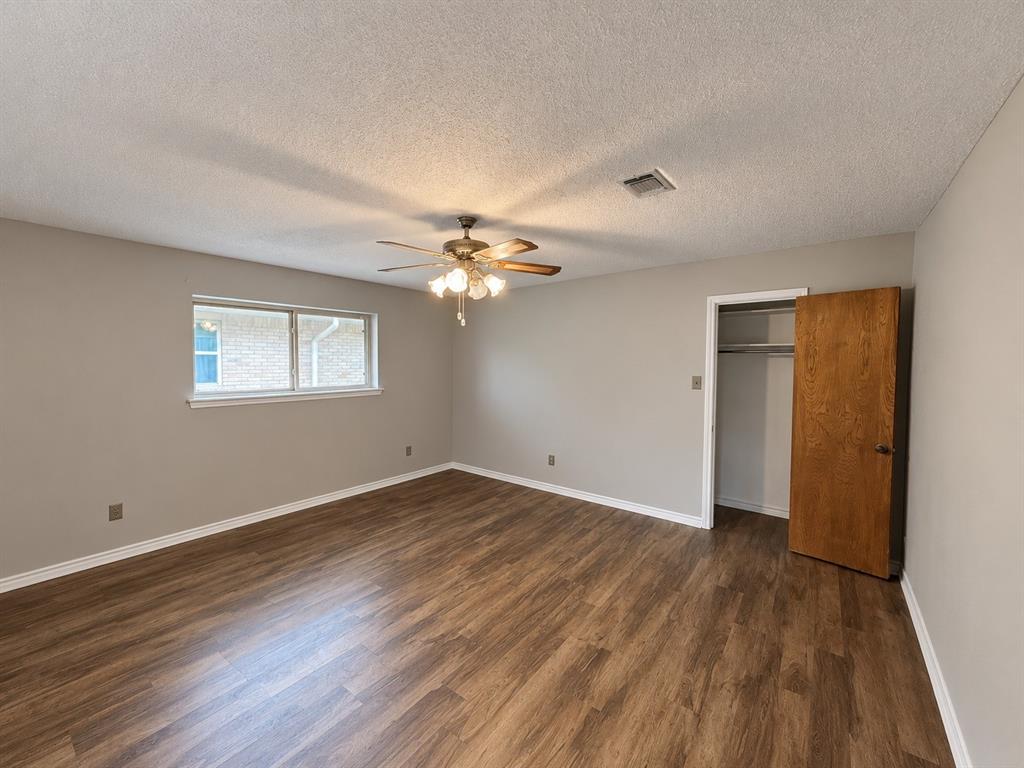 Interior room featuring wood-finish flooring, neutral wall paint, a ceiling fan with integrated lighting, and a closet with a wooden door Interior room featuring wood-finish flooring, neutral wall paint, a ceiling fan with integrated lighting, and a closet with a wooden door