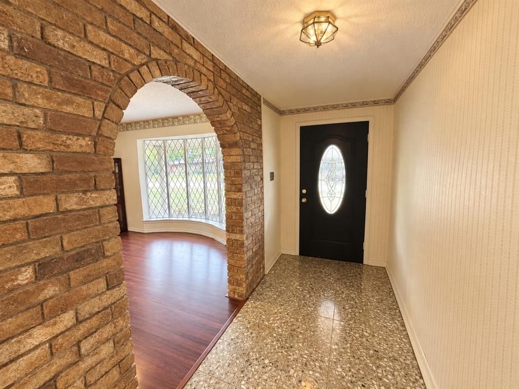 Entryway featuring a structural brick arch, diamond-pane bay window, solid-core front door with decorative oval glass inlay, wood-finish flooring, and terrazzo tile flooring
