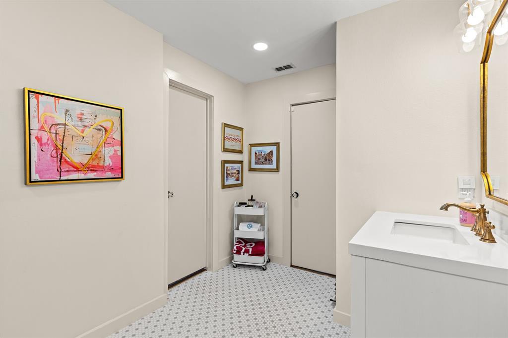 Bathroom featuring a white vanity cabinet, rectangular under-mount sink, brass finish widespread faucet, and geometric-patterned tile flooring