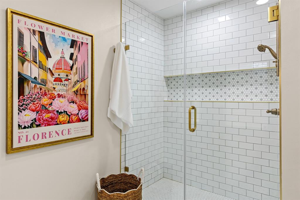 Walk-in shower featuring white subway wall tile, a geometric-patterned tile niche, brass-finish hardware, and a frameless glass door